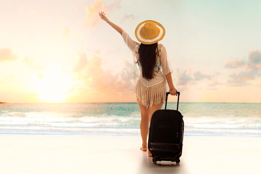 Rear view of tourist woman standing on beach with a suitcase