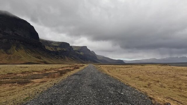 Gravel track along base of Lomagnupur cliff wall with Skeidararsandur outwash plain stretching right, Iceland