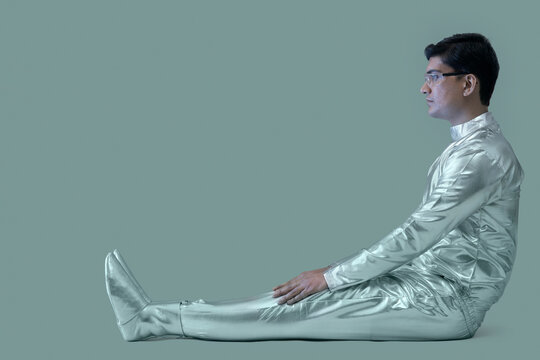 side view of a man wearing silver dress sitting on a grey backdrop,future technology concept. 