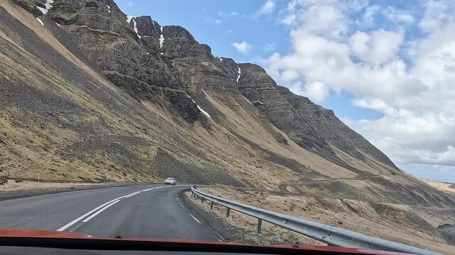 Dashcam POV driving Route 47 along Hvalfjordur fjord with towering layered basalt mountain wall, Iceland