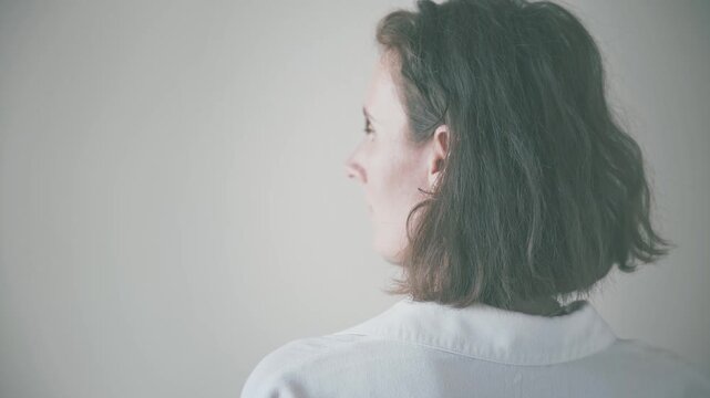 Rear view of woman with short, tousled hair in light collared top, calm posture in minimalist indoor setting with soft daylight, perfect for wellness and lifestyle themes.