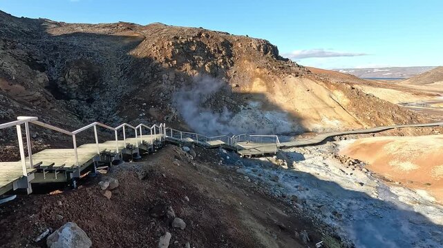 Wooden staircase and viewing platform at Seltun geothermal area with steam vent and coloured hills beyond, Iceland