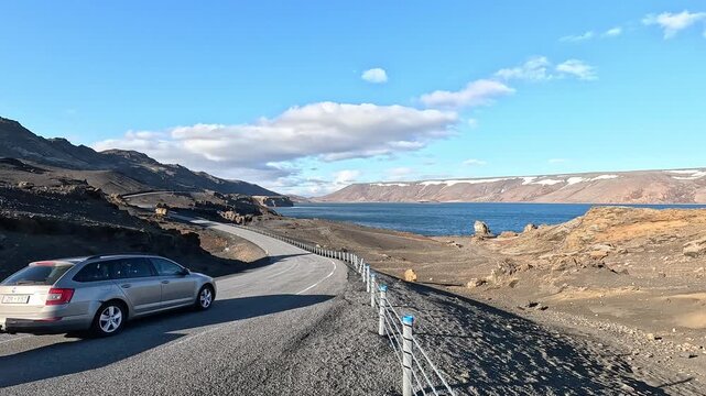 Car parked on Route 42 beside Lake Kleifarvatn with black lava shore, deep blue water and snow-dusted cliffs, Iceland