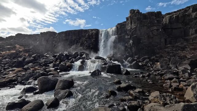 Oxararfoss waterfall frontal wide shot cascading over basalt rift wall into rocky river, Thingvellir National Park, Iceland