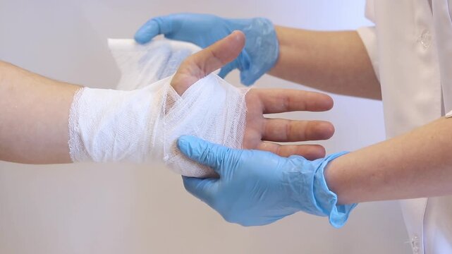 A medical worker in blue gloves applies a sterile gauze bandage to a patient's wrist. First aid for an injury. Close-up of the process of bandaging a hand in a medical institution. Healthcare concept