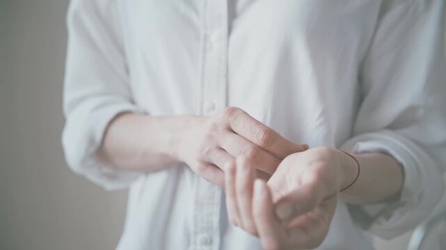 Close up of person adjusting red string bracelet on wrist indoors, rolled sleeve, soft diffused light, shallow depth of field, copy space