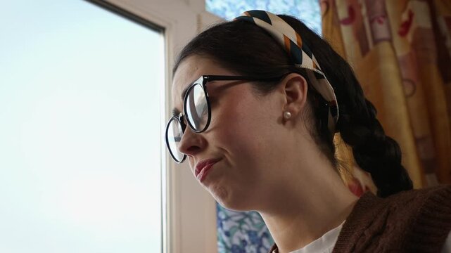 Young Caucasian woman works thoughtfully with an upset and frustrated expression while studying remotely at home. Emotional stress and difficulties during online learning and professional tasks.