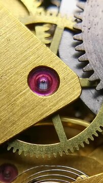 Vertical extreme close up of an antique watch mechanism featuring a ruby jewel bearing and interlocking rotating gear wheels.