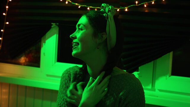 Young Caucasian woman sitting shyly at a party, gently swaying to the music and hesitantly trying to greet someone. Colorful lights illuminate the room, creating a festive atmosphere