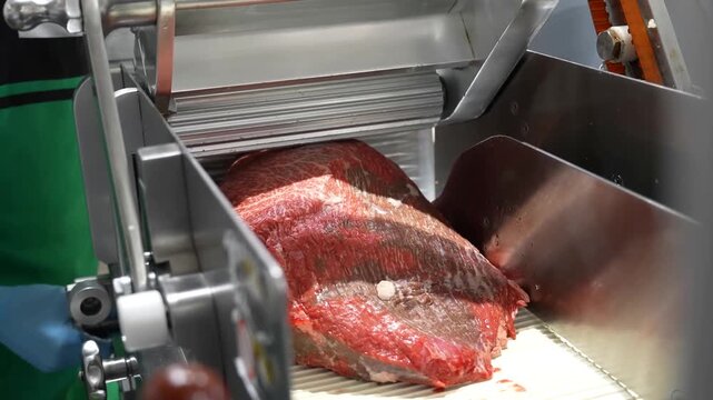 Industrial processing of raw beef steaks for retail sales in a commercial butcher setting involves expert handling to ensure uniform slice thickness for cooking