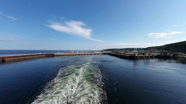 Harbor infrastructure frames a vessel's departure as propeller wash creates textured patterns on calm water.