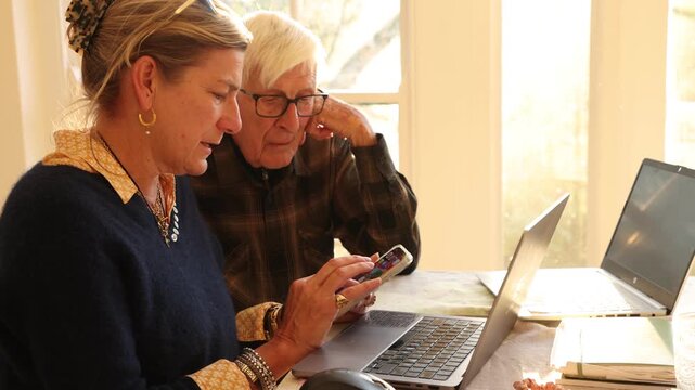 adult daughter helping her elderly father with his finances using laptop