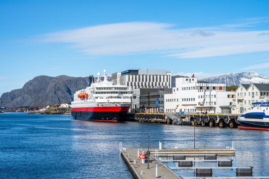 Ships are docked at Bronnoysund harbor in Norway with buildings and mountains in the background on a clear day