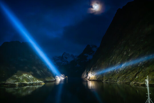 The entrance to Trollfjord in Norway, seen from the water and illuminated by large searchlights at midnight