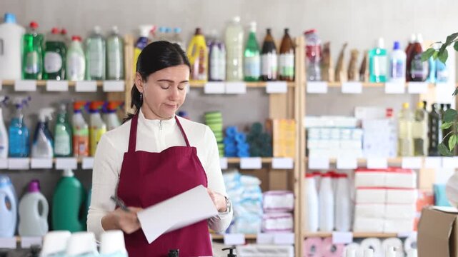 Trainee saleswoman reacts emotionally to the paperwork, she is irritated and dissatisfied. Woman experiences burnout at work. Salesperson works with papers in the warehouse of a household compartment