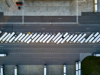 Top down aerial view of many white semi trucks parked in a neat row at a modern logistics center, fleet management and global freight transportation concept. © JaRu Creative Studio