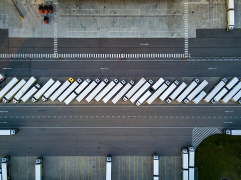 Top down aerial view of many white semi trucks parked in a neat row at a modern logistics center, fleet management and global freight transportation concept.