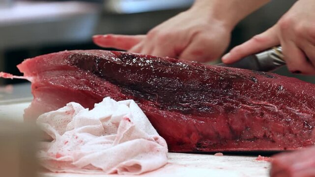 A skilled worker performs the precise slicing of a fresh tuna fish on a clean table while highlighting the deep red meat texture and the anatomical structure of the large ocean catch