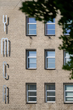 Brick facade of the historic YMCA building featuring vertical metal lettering with tree branches in the foreground, Gdynia, Pomerania, Poland, Europe
