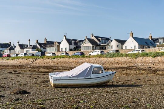 White boat rests on exposed shore of Findhorn Bay with houses and cars in Findhorn, Moray, Scotland