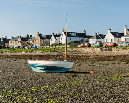 Small boat on Findhorn Bay shore with village houses in background on a clear day in Moray Scotland