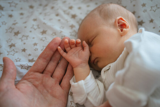 Newborn baby holding adult's hand while sleeping, symbolizing protection, love, connection, and family bonding during early childhood development