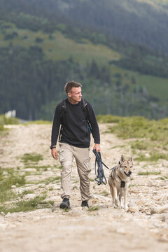 Young man hiking with his Czechoslovakian Wolfdog on a mountain trail, active pet travel and outdoor companion lifestyle