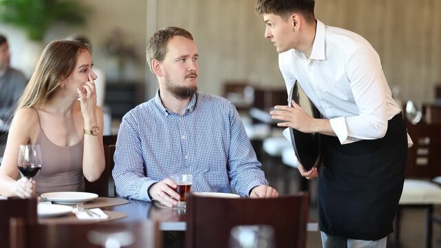 Couple resting, sitting in restaurant and ordering food. Waiter guy tells young women visitors of cafe about dish from chef. High quality 4k footage