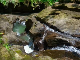 Water flowing between dark volcanic rocks forming natural pools and cascades viewed from above in tropical river © dvad