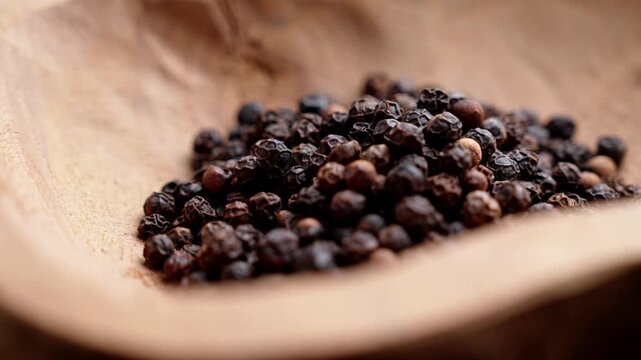 Whole black peppercorns (Piper nigrum) piled inside an authentic rustic wooden bowl. Wrinkled texture of the spice. Rotation