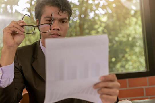 Tired businessman taking off glasses with eye pain during working and reading paperwork in office. Selected focus