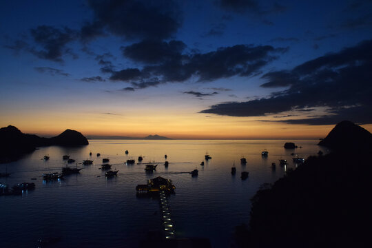 Sunset at Labuan Bajo harbor with a small boat docked on the beach as the sun sets over the edge of the sea.