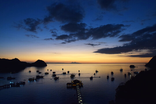 Sunset at Labuan Bajo harbor with a small boat docked on the beach as the sun sets over the edge of the sea.