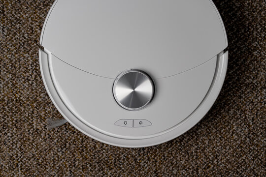 White robot vacuum cleaner top view on carpet, closeup. Smart robotic vacuum cleaner on home carpet with lidar sensor and control buttons. Modern domestic appliance concept