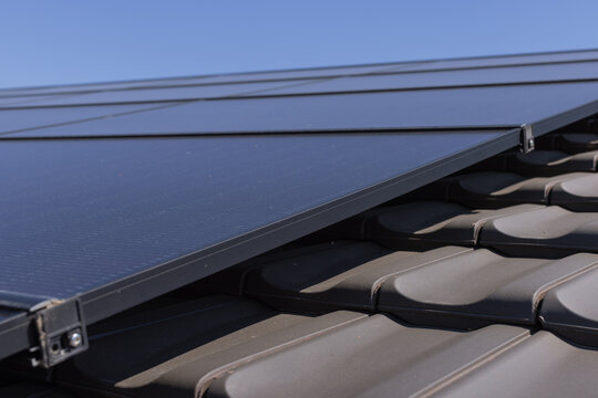 close-up shot of photovoltaic panels next to roof tiles and in front of blue sky
