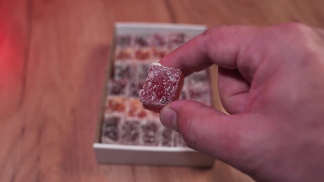 In the fingers of the oriental sweet Turkish delight on the background of a box of sweets. Very sweet, lots of sugar, natural product, eco-friendly sweets.