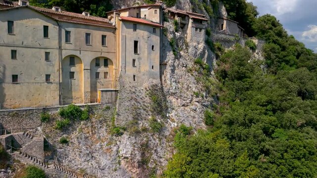 Greccio Sanctuary Italy 4K Drone. Cinematic 70mm flight of historic cliffside monastery built into rock. Saint Francis of Assisi sacred pilgrimage site in Rieti mountains b roll video asset