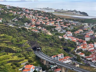 Scenic panoramic view of Madeira Island, Portugal, featuring a dramatic highway bridge emerging from a mountain tunnel above a coastal village © Kate Ra