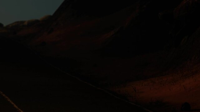 The scene shows a mountain landscape during dusk. Shadows cast over the ground and rock formations create a feeling of depth. The fading light highlights the terrain.