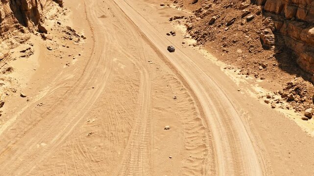High angle aerial view of a single car driving through a narrow canyon in the desert terrain of Xinjiang, China.