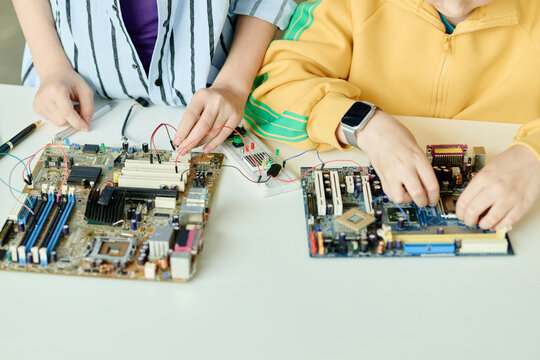 Close up of teenagers assembling computer motherboards and testing circuits at desk, learning electronics and hardware skills. Ideal for STEM education, coding camp, tech training