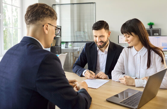 Couple clients meet manager for finance investment consultation. They complete agreement, signing a contract during a professional meeting with laptop on desk. Concept of commitment and trust.