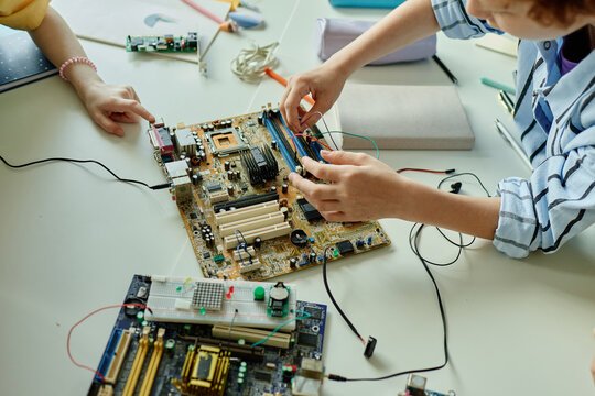 Close up of schoolchildren assembling computer motherboard and testing electronic components during STEM lesson. Image supporting coding education, robotics workshop, tech training
