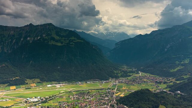 Rushing clouds over Interlaken valley town and Swiss Alps mountain peaks in dramatic summer time lapse video with panoramic green landscape view
