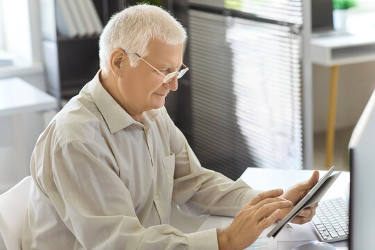 Senior man with tablet accountant analyzing financial report. Analyst works in a tidy office, reviewing data on laptop and planning budgets. Concepts include finance and digital productivity.