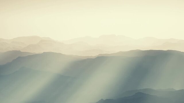 A view of distant mountains with layers of hills visible. Light beams shine through the scene. The landscape shows varying shades and shapes in the daytime.