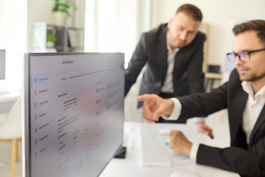 Executives in office meeting discuss data analytics. Managers point at a dashboard, reviewing reports and metrics. Clean corporate business supports teamwork and strategy for a presentation.