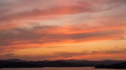 Obraz premium Vibrant sunset over calm waters with silhouetted mountains