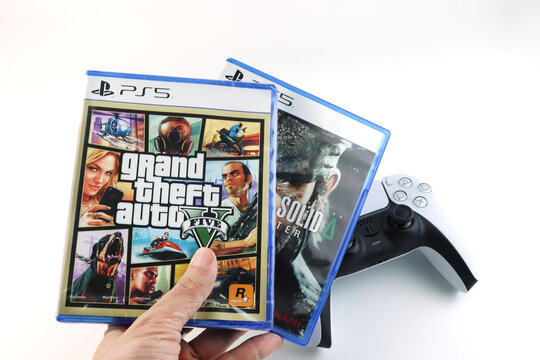 Grand Theft Auto V (GTA 5) PlayStation 5 game case held in hand with  background of PS5 DualSense controller Modern gaming popular console title, entertainment, technology, and video game collection.