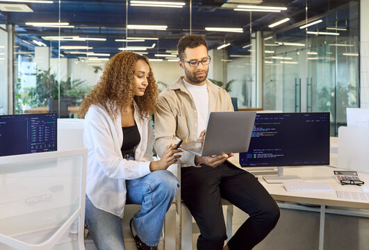 Colleagues teamwork on laptop during office discussion. Developers review coding tasks and training using collaboration technology in a modern workspace. Clear concept of digital teamwork.